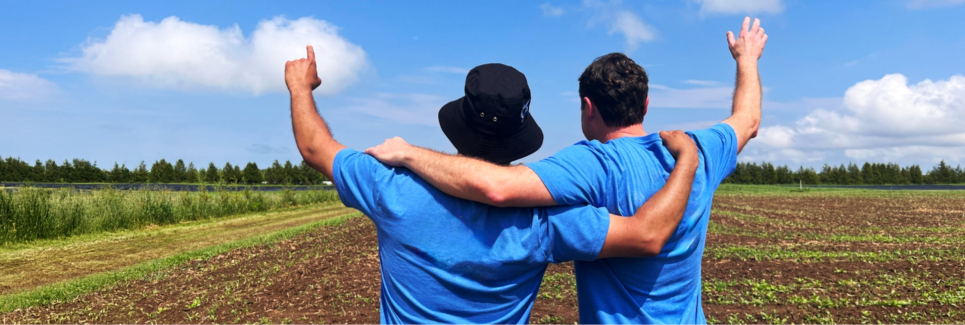 Two men stand in the middle of a field and clear blue skies with am arm on each other's shoulders with the other arm reaching upwards to the sky. Two men stand in the middle of a field and clear blue skies with am arm on each other's shoulders with the other arm reaching upwards to the sky.