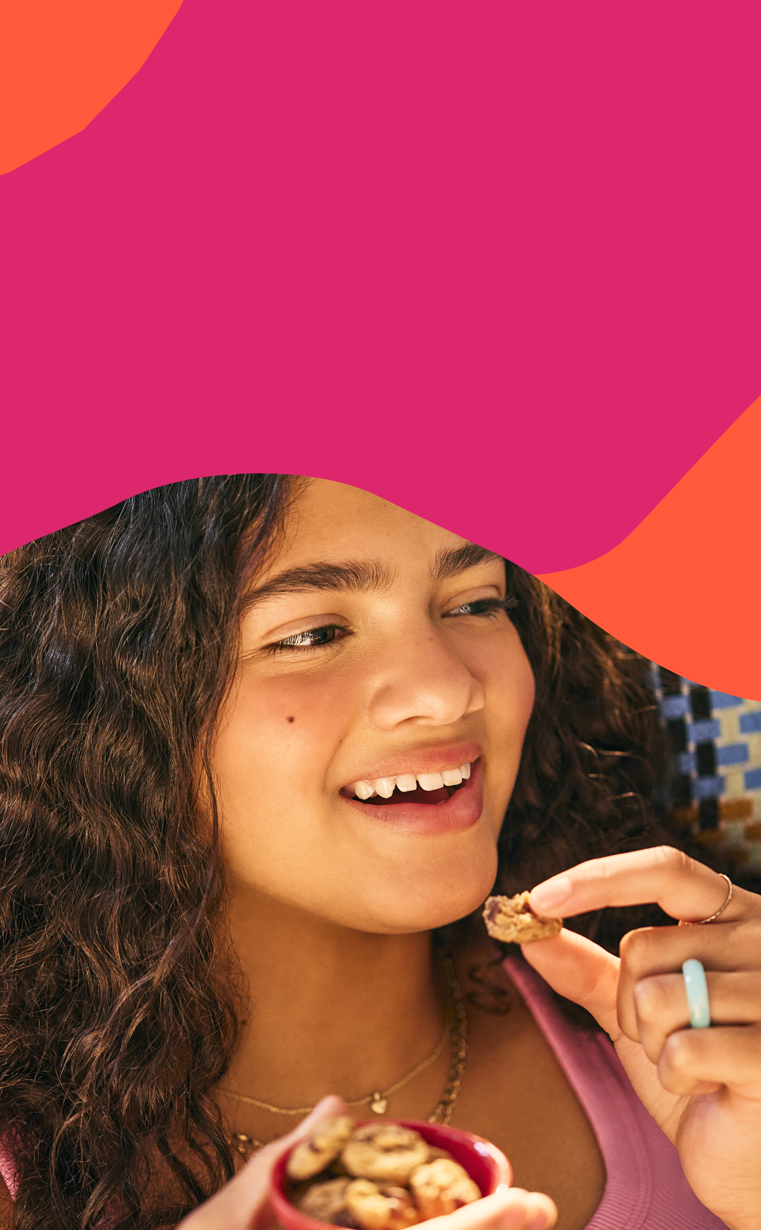Girl eating MadeGood soft baked cookies on a pink and orange abstract background. Girl eating MadeGood soft baked cookies on a pink and orange abstract background.