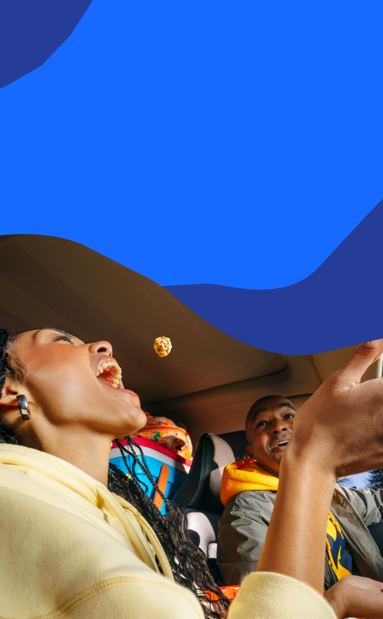 Woman eating popcorn in a car with a man beside her on a blue abstract background