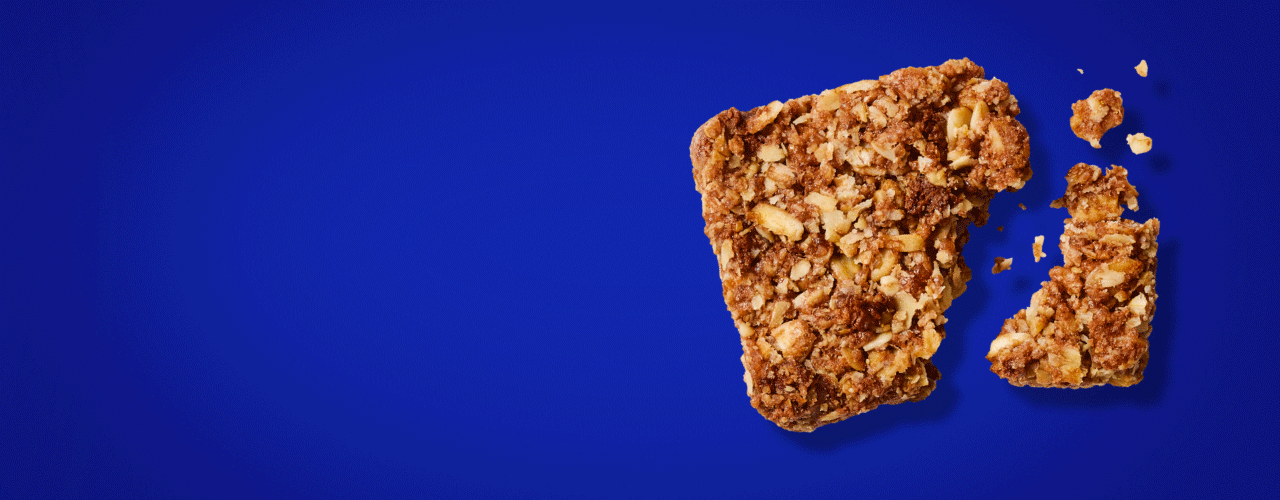 A MadeGood bar piece with oats and dark chocolate in it on a blue background