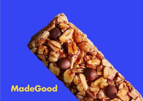 A granola bar with nuts and chocolate chips is displayed on a vibrant blue background. The text “MadeGood” is in yellow at the bottom left.