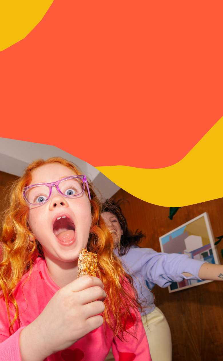 Child with red hair and pink glasses holding a granola bar against a colorful background abstract background