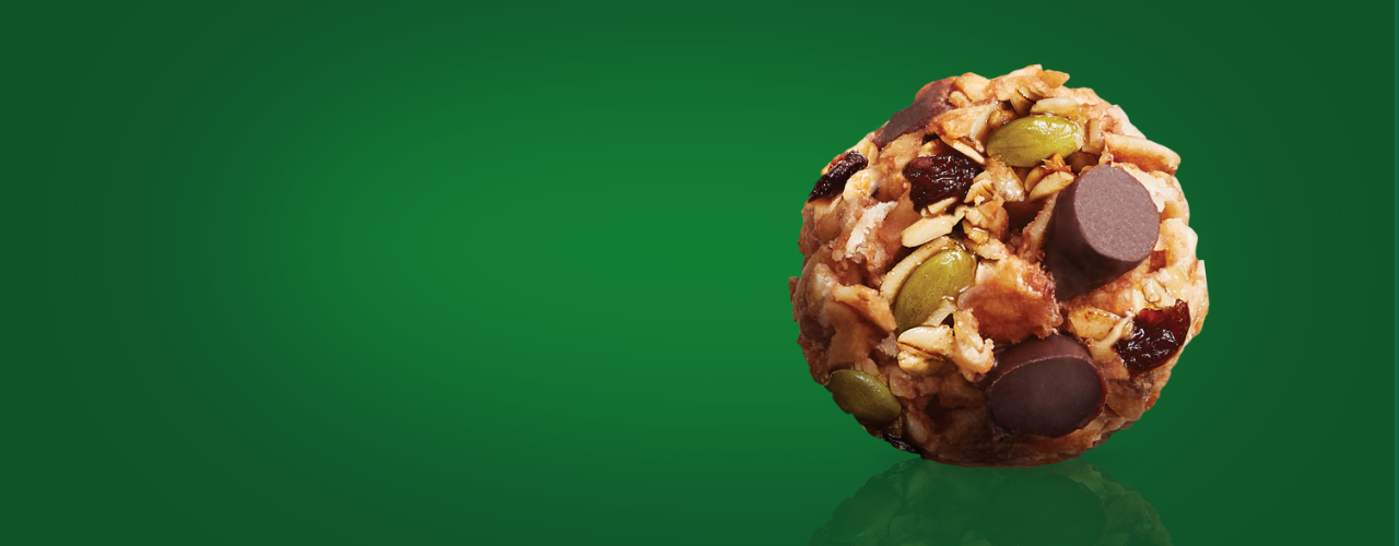 A MadeGood trail mix bite with chocolate chips, pumpkin seeds, raisins, dried cranberries, and sunflower seed butter