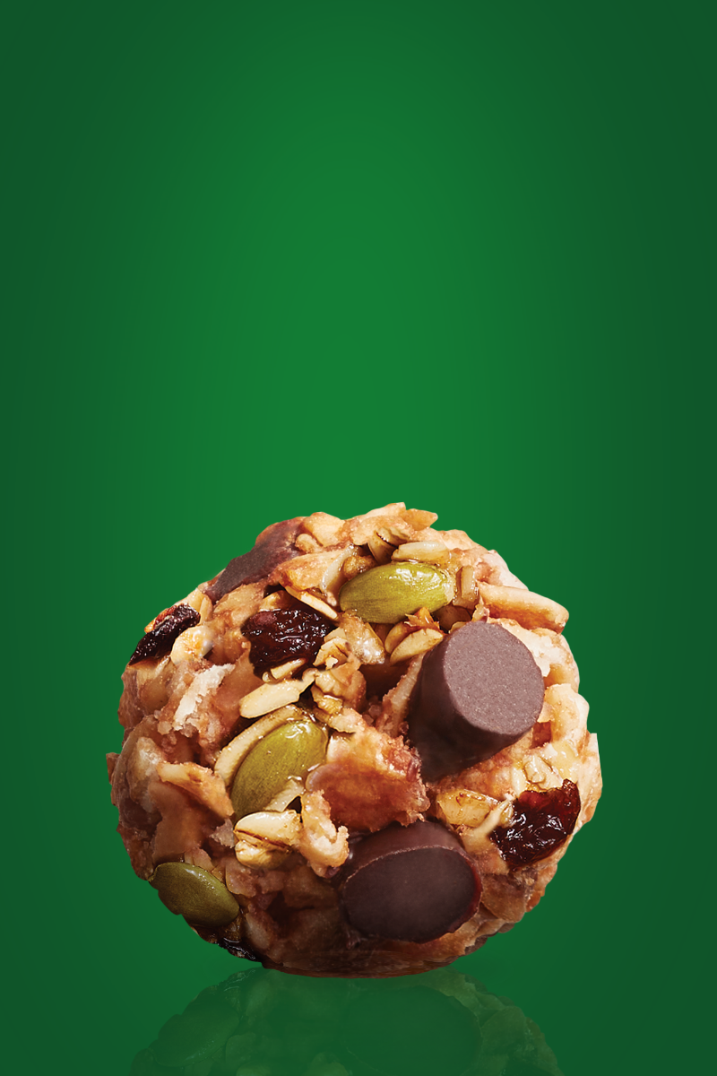 A MadeGood trail mix bite with chocolate chips, pumpkin seeds, raisins, dried cranberries, and sunflower seed butter.